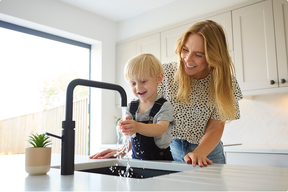 Kind wast zijn handen in de keuken terwijl moeder toekijkt Kind wast zijn handen in de keuken terwijl moeder toekijkt